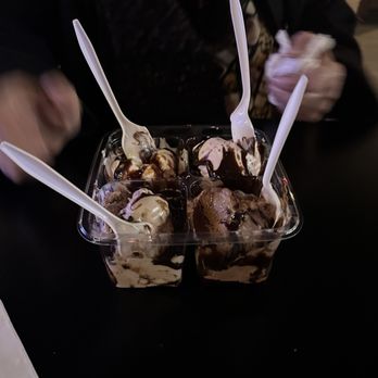 Lickety Splitz - Flight - Four small cups of ice cream with chocolate syrup and toppings, each with a plastic spoon, are placed on a dark surface. - Ice Cream & Frozen Yogurt Near Me - Maple Shade, New Jersey