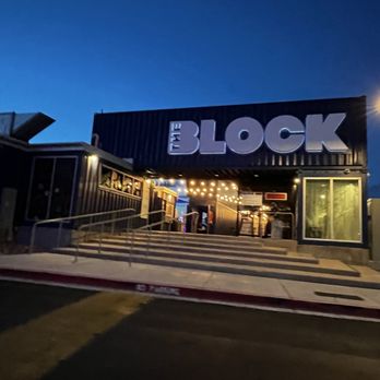 The Block - The photo shows the exterior of The Block business, with a large sign displaying the name. The entrance area is lit with string lights, and the building appears to be made of dark-colored materials. The sky is dark, indicating it is evening or night. The sidewalk and ramp leading to the entrance are visible, with no people present. - Shopping Centers Near Me - Rio Rancho, New Mexico
