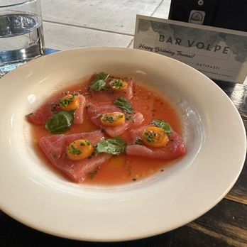 Bar Volpe - Crudo di Tonno - A dish of crudo di tonno, featuring thinly sliced raw tuna, garnished with basil leaves and dollops of egg yolk, served on a white plate at Bar Volpe. - Italian Near Me - Boston, Massachusetts
