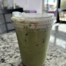 Blueberry Lavender Matcha - A clear plastic cup containing a green matcha drink with ice, placed on a granite table inside a cafe.