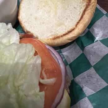 McBride's North - Toasted bun - A sandwich featuring lettuce, tomato, onion, and cheese on a bun, with a toasted bun in the background, on green checkered paper. - Pubs Near Me - Aurora, Illinois