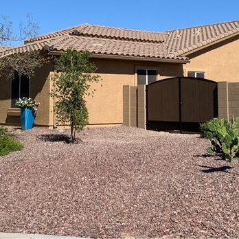 Victory Construction - A single-story house with a tan exterior, surrounded by a desert-style yard with gravel, small trees, and cacti, enclosed by a brown fence. - Masonry/Concrete Near Me - Phoenix, Arizona