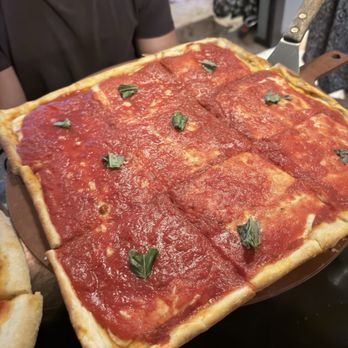 Villa Capri - Nonnas Pizza - A rectangular pizza with tomato sauce and basil leaves, served on a wooden pizza peel, with a person in a dark shirt visible in the background. - Pizza Near Me - Doylestown, Pennsylvania