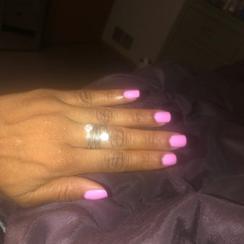 Beautiful Nails - The image shows a hand with neatly painted pink nails resting on dark, possibly satin or silk fabric. The hand is adorned with a silver ring featuring a clear gemstone. The background includes furniture such as a dresser and a chest of drawers, with a vent visible on the wall. The lighting is dim, and the focus is on the hand and nails. - Nail Salons Near Me - Crest Hill, Illinois