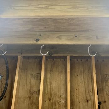 Pro Quality - Bike hooks - A wooden wall with four white hooks mounted on a wooden beam, with a bicycle wheel hanging on the left side, in a workshop or storage space. - Handyman Near Me