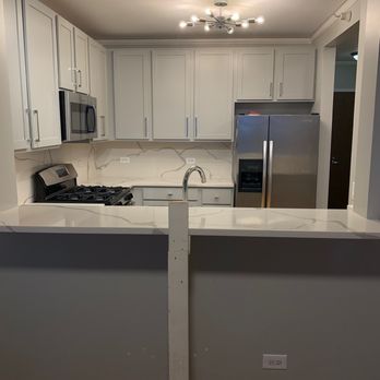 Crespo Granite - The after! - A kitchen featuring white cabinetry, stainless steel refrigerator and microwave, a gas stove, and a marble backsplash. The space is illuminated by a ceiling light fixture. - Countertop Installation Near Me - Chicago, Illinois