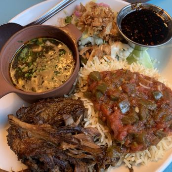 Centro Mexican Kitchen - Tacos de Birria (Stewed Beef Tacos) - A plate of Mexican cuisine includes a serving of white rice topped with a tomato-based sauce containing chopped green peppers. Accompanying the rice is shredded beef, a small bowl of dark soy or similar sauce, a small pitcher of broth or soup with herbs, and a side of chopped vegetables and fried onions. The dish is presented on a white plate with a metal spoon and a brown tray in the background. - Mexican Near Me - Boulder, Colorado