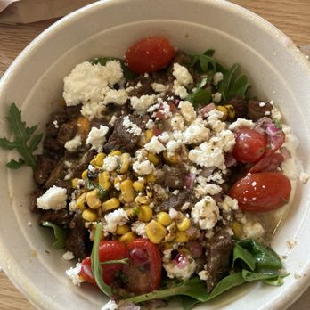 CAVA - A salad bowl contains cherry tomatoes, corn, crumbled cheese, and mixed greens, served in a disposable bowl at a restaurant. - Mediterranean Near Me - Newington, Connecticut