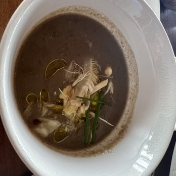 Canoe - Wild Mushroom Soup - A bowl of dark-colored mushroom soup garnished with seafood, herbs, and oil droplets, served in a white bowl. - Canadian (New) Near Me - Toronto, Ontario