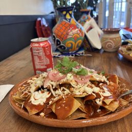 Red Chile Chilaquiles - A dish of red chile chilaquiles topped with cheese, sliced onions, and cilantro is served on a ceramic plate at Cafe es Amor in Albuquerque.