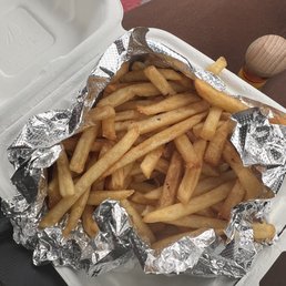Skinny fries!!! - A serving of French fries in a foil-lined container on a white tray, with a brown cloth and a small wooden object in the background.