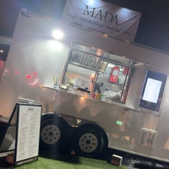 Mada Eatery - Food truck - A food truck with a serving window and menu board is parked on a gravel surface, featuring a small artificial grass mat in front. The truck is part of a business offering halal fusion cuisine. - American Near Me - Everett, Massachusetts