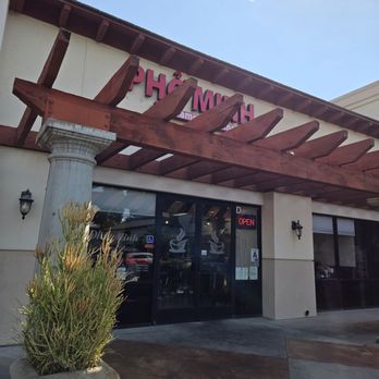 Pho Minh - Storefront - A cafe storefront features a wooden pergola, glass doors with coffee cup graphics, and an 'OPEN' sign, with a potted plant outside. - Soup Near Me - Temecula, California