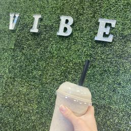 a person holding a drink in front of a wall with the word vibe