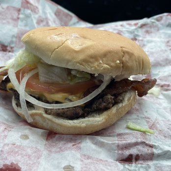 Big Ass Burgers - Little Ass Burger - A burger with bacon, lettuce, tomato, onion, and cheese on a bun, placed on checkered paper in a vehicle. - Fast Food Near Me - Thoreau, New Mexico