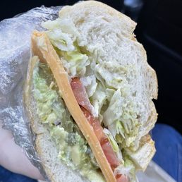 Avocado and cheese sandwich with tomato, pickles, lettuce on a sourdough roll