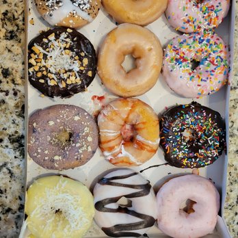 Duck Donuts - A box contains twelve donuts with different toppings, glazes, and sprinkles, arranged in three rows on a white tray. - Donuts Near Me - Moosic, Pennsylvania