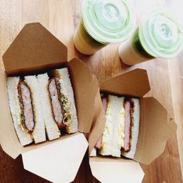 Chicken Katsu Sando - Two cardboard takeout boxes containing sandwiches and two cups with green lids are placed on a wooden table.