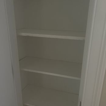 White Pine Builds - Shelving - The image shows an empty built-in closet painted white, featuring four horizontal shelves. The closet is open, revealing its interior space with no items stored inside. The door frame and part of the door are visible on the right side of the image. The closet appears to be in a residential setting, ready for use or storage. - Handyman Near Me