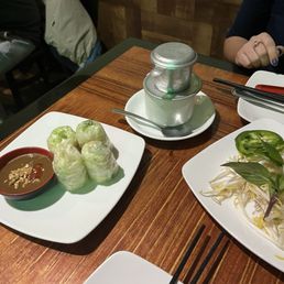 summer rolls - Four fresh spring rolls with a dipping sauce are placed on a white plate at a Vietnamese restaurant table.