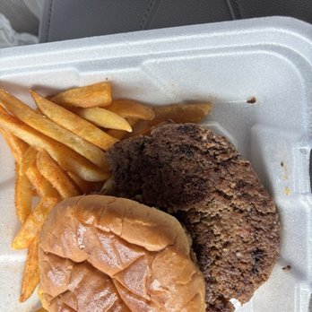 Daddy Shark - Kids Cheeseburger - A foam takeout container holds a cheeseburger with a soft bun, accompanied by a portion of French fries and a fried chicken patty. The fries are seasoned and placed beside the burger, which appears to be assembled with a beef patty, cheese, and toppings. The image suggests a casual meal, likely from a fast-food or takeout restaurant. - Seafood Near Me - Clinton, Mississippi