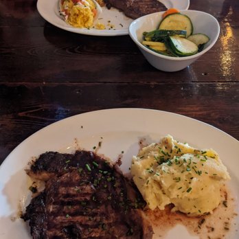 The Dish Room - In the back- KC strip steak w/ side of vegetables & sweet corn tamale. In front is ribeye w/ side of mashed potatoes. - New American Near Me - Burlington, Colorado