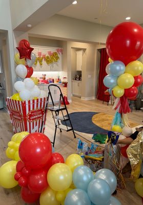 Carnival Birthday Party Decor for In/Outdoors - This Balloon project was for an in/outdoor carnival themed birthday party. A Balloon Garland adorned the lighting fixtures in the kitchen. Jumbo Spiked tassel columns stood guard outside the front door.  Balloons were used to mimic popcorn in a giant striped bucket. Balloon Letters were used to display a message to visitors and more floor balloon bouquets were placed throughout the house to continue the custom carnival theme and colors. Our customer was very satisfied with our work and you can read more about their review here on our Yelp page!