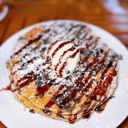 Hershey Pantry - Oreo Pancakes: two pancakes with crumbled Oreos, topped with sweet cream cheese, chocolate syrup, powdered sugar, served with bacon