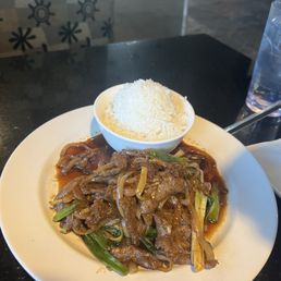Bulgogi - A dish of beef stir-fry with vegetables and sauce, accompanied by a bowl of white rice, on a black table at a restaurant.