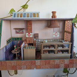Bagel diorama - A detailed miniature bakery scene featuring a seating nook, display case with baked goods, and signs for ordering and pickup, set inside a small model building.
