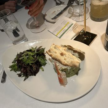 Cafe Central - A white plate with a layered dish topped with a crispy bread piece, accompanied by a mixed green salad, on a restaurant table. - Salad Near Me - El Paso, Texas