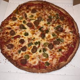 Gluten Free Pizza - A pizza topped with sausage, green peppers, and melted cheese, served in a pizza box, with a slightly irregular round shape.