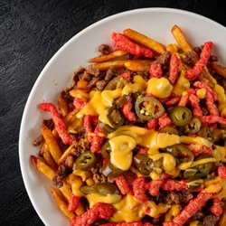 Fuego Cravings - Close up of crispy seasoned fries loaded with rich nacho cheese, your choice of meat, spicy Hot Cheetos, and jalapeños.