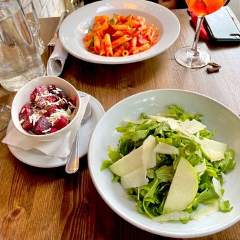 Follia - a woman sitting at a table with two plates of food - Wine Bars Near Me - New York, New York Follia - a woman sitting at a table with two plates of food - Wine Bars Near Me - New York, New York
