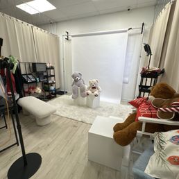 A photo studio setup featuring teddy bears, a white backdrop, and various props, with lighting equipment and curtains.