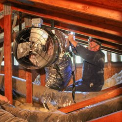 Inside the attic, Mark attaches the QuietCool whole house fan to the rafters with metal straps.