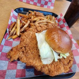 Large breaded Pork Tenderloin and it melted in my mouth!!! So very tender and absolutely delicious!! - A tray holds a large fried chicken fillet with French fries and a sandwich with lettuce and a bun, served with a soda.