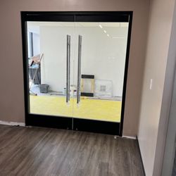 JBI Commercial Openings - A pair of modern frameless glass double doors with long, vertical stainless steel handles installed in a commercial interior....