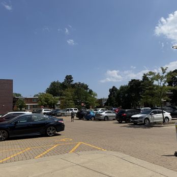 Target - Their convenient but smallish parking lot. - A parking lot with numerous parked cars of different makes and colors, including black, white, and red vehicles. The lot has marked parking spaces and a pedestrian crossing sign on a stand. The background features trees, residential buildings, and a bright, partly cloudy sky. The scene is well-lit with natural sunlight, indicating daytime. - Department Stores Near Me - Skokie, Illinois