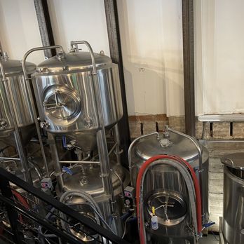 Perspective Brewing - Vats - A set of stainless steel brewing tanks is positioned against a wall in a brewery, with some tanks connected by pipes and valves. The background features brick and drywall walls, indicating an industrial or renovated space. The tanks are used for brewing craft beer or similar beverages. - Brewpubs Near Me - West Allis, Wisconsin