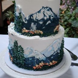 A wedding cake decorated with mountains, trees and flowers.