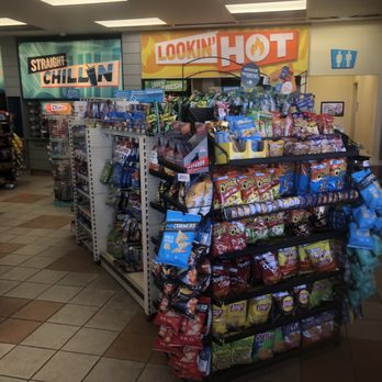 ampm - a grocery store - A snack display rack filled with various chips and snack bags is situated inside a convenience store, with signage above promoting hot and cold items. - Convenience Stores Near Me - Turlock, California