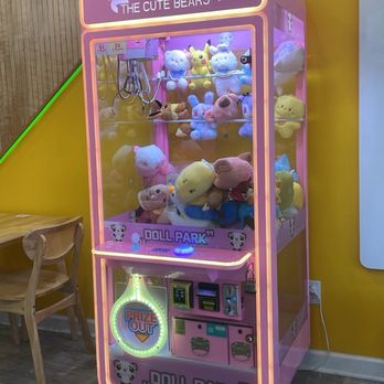 Sip Munch Cafe - A pink claw machine filled with plush toys, located in a gift shop named 'The Cute Bears,' with a yellow wall and wooden floor. - Coffee & Tea Near Me - Austin, Texas