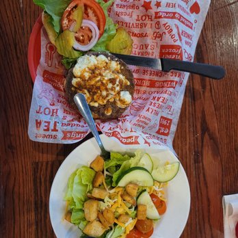 Jefferson's - Blue Cheese Burger w Side Salad - A burger topped with cheese and sauce, served with a side salad containing lettuce, cucumber, cherry tomatoes, shredded cheese, and croutons, on a wooden table. - American Near Me - Lawrence, Kansas