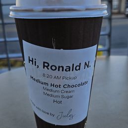 Hot  Chocolate made for me - A paper cup of hot chocolate with a personalized label addressed to Ronald N., placed on a table outdoors.