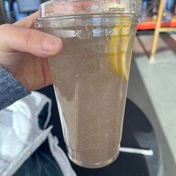 Fall River Heritage State Park - Lemonade - A person holds a plastic cup filled with a cold, light-colored beverage with a lemon slice inside, in a busy indoor setting. - Parks Near Me - Fall River, Massachusetts