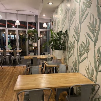 Stocked Cafe - Interior - A cafe interior featuring wooden tables, metal chairs, and a wall decorated with botanical wallpaper, illuminated by ceiling and pendant lights. - New American Near Me - Brooklyn, New York