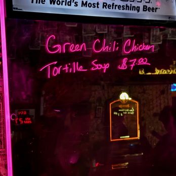 Western Bar & Cafe - a neon sign - Pink neon sign in a bar or cafe advertises 'Green Chili Chicken Tortilla Soup' for $7.00. The sign is reflected on a glass surface, with a Coors Light advertisement above and a dimly lit interior visible in the background. The setting appears casual with a focus on food and drink offerings. - American Near Me - Cloudcroft, New Mexico