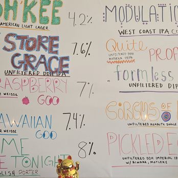Knotted Root Brewing - A whiteboard showcases a list of beers with their names, styles, and alcohol percentages, written in colorful marker with varied fonts and styles. Some beers include 'Oh Kee', 'Toy Store Grace', 'Raspberry Goo', and 'Hawaiian Goo', with styles like American Light Lager, Unfiltered DIPA, and English Porter. Additional notes and descriptions are included, along with decorative elements such as a rainbow and a small Maneki-neko figurine at the bottom of the board. The overall presentation is vibrant and informal, typical of a brewery or taproom menu. - Breweries Near Me - Nederland, Colorado