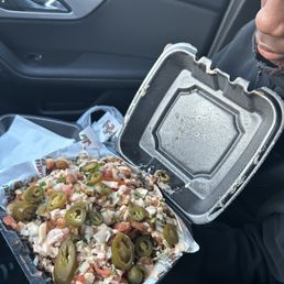 Fiesta Salad Bowl - A person in a car holds a takeout container filled with loaded nachos topped with jalapeños, sour cream, and other toppings.